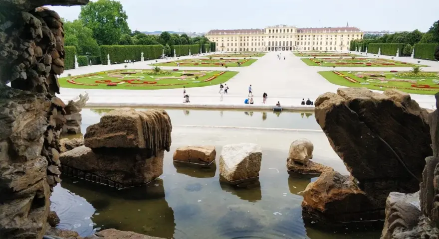 Wiedeń ogrody Sisi: malowniczy widok na pałac Schönbrunn i jego kwieciste tarasy, z kamienną fontanną w pierwszym planie.