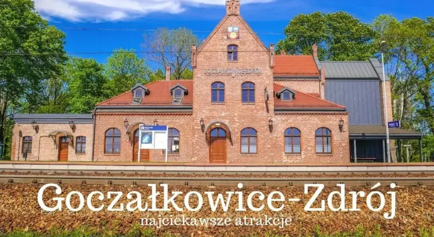 Ceglana stacja kolejowa Goczałkowice-Zdrój z czerwonym dachem i zielonymi drzewami w tle.