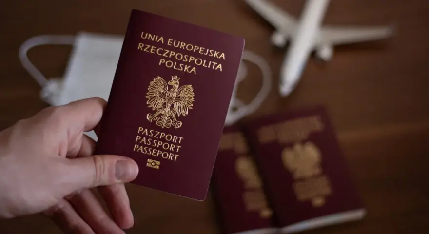 Dłoń trzyma polski paszport. Obok leżą kolejne dokumenty, maseczka i model samolotu. Zastanawiasz się, ile trwa wyrobienie paszportu?
