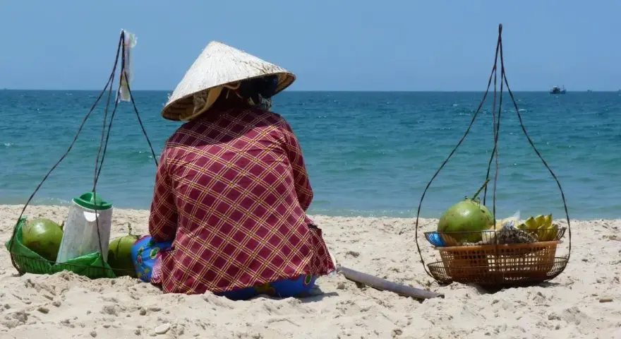 Sprzedawczyni kokosów na plaży w Mui Ne, Wietnam. W tle błękitne morze i niebo.