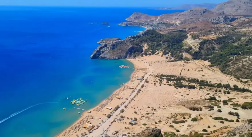 Widok z lotu ptaka na piaszczystą plażę z leżakami, turkusowe morze i górzysty krajobraz Rodos.