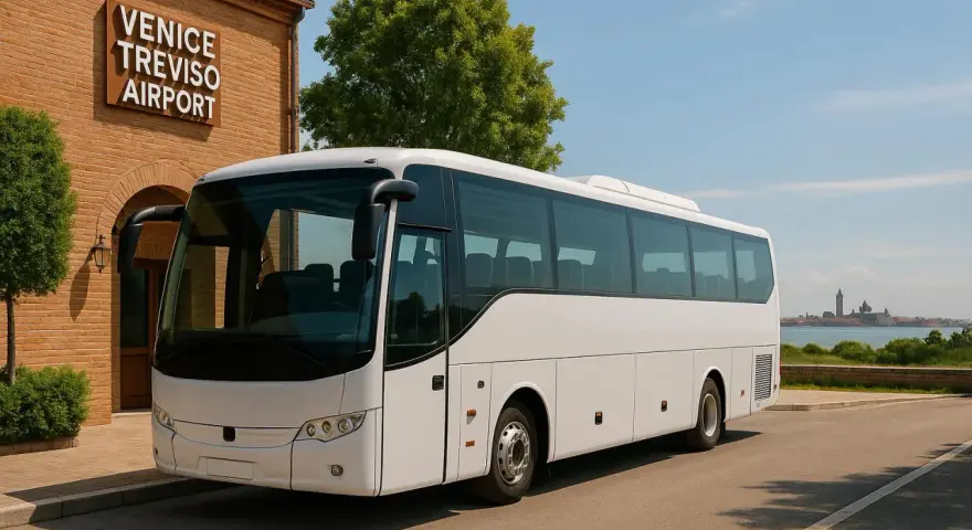 Biały autokar czeka na pasażerów przy budynku z napisem VENICE TREVISO AIRPORT. W tle widać panoramę Wenecji.