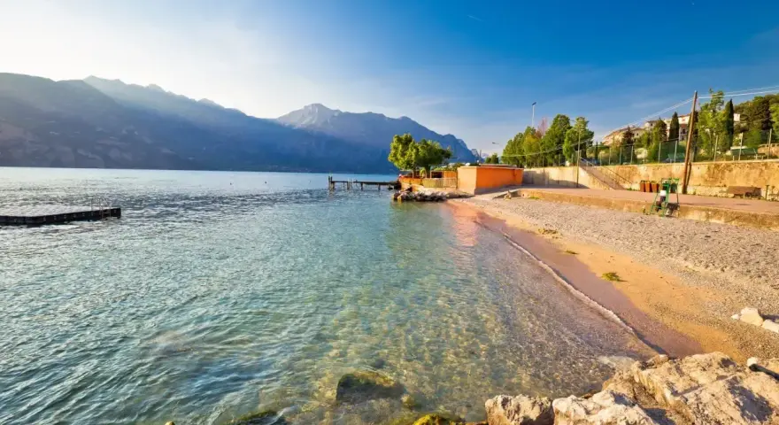 Słoneczna plaża nad jeziorem Garda z kamienistym brzegiem i łagodnymi falami.