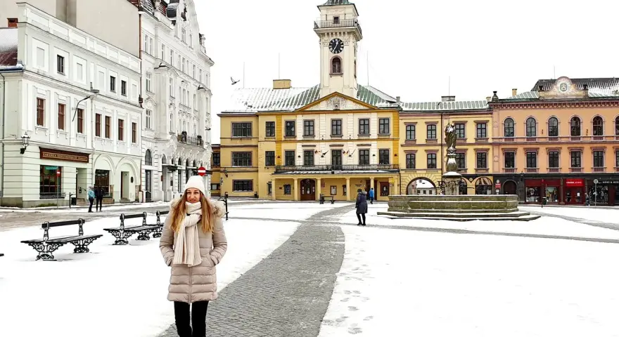 Zimowy spacer po Rynku w Cieszynie. Kobieta w ciepłym ubraniu przemierza ośnieżony plac, podziwiając zabytkowe kamienice i ratusz. Idealny pomysł na cieszyn w jeden dzień.