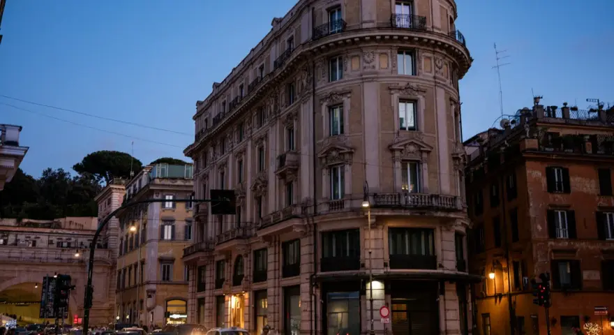 Wieczorna ulica w Rzymie z zabytkowymi budynkami i ruchem ulicznym.