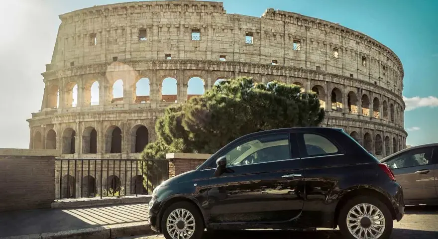 Czarny Fiat 500 pod Koloseum w Rzymie. Zastanawiasz się, ile się jedzie z Polski do Włoch samochodem?
