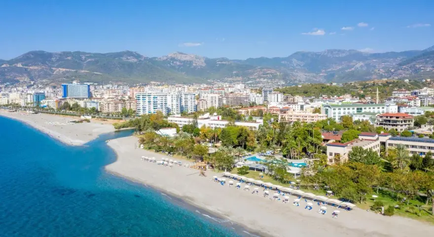 Widok z lotu ptaka na kurort nad morzem w Turcji z plażą, hotelami i górami w tle.
