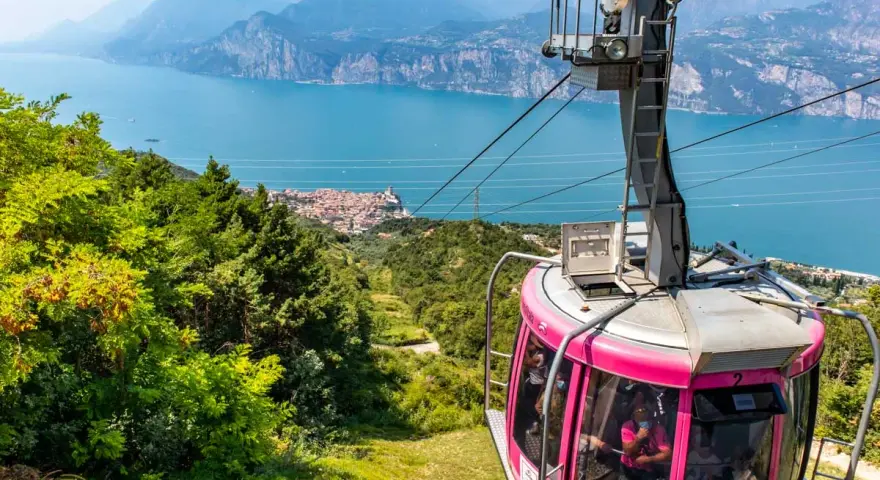 Różowa kolejka linowa Monte Baldo zjeżdża w dół, oferując widok na jezioro Garda i malownicze miasteczko.