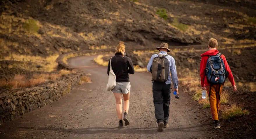 Trzy osoby wędrują po wulkanicznym krajobrazie Sycylii. Styczeń na wyspie oferuje przyjemną temperaturę do trekkingu.