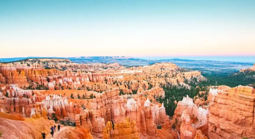 Zachód słońca nad Bryce National Park. Wąwóz pełen pomarańczowych hoodoos i zielonych drzew, z turystami na szlaku.