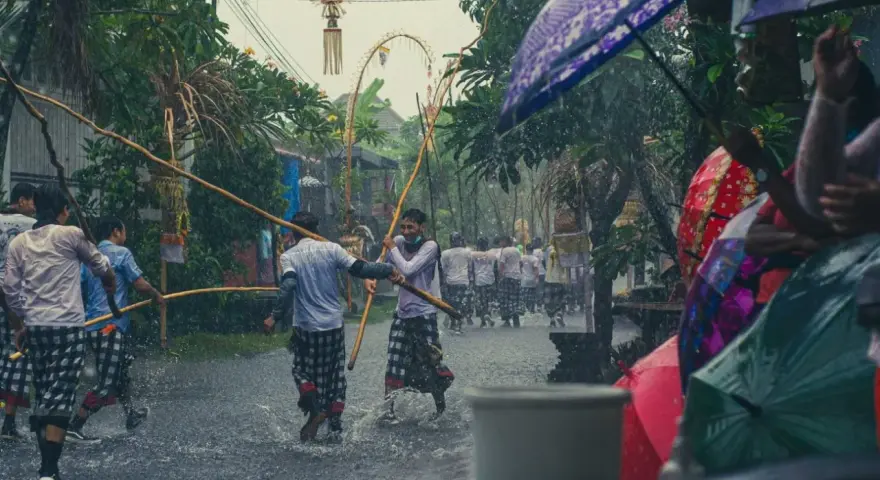 Procesja w deszczu na Bali, ludzie z parasolami i bambusowymi tyczkami.