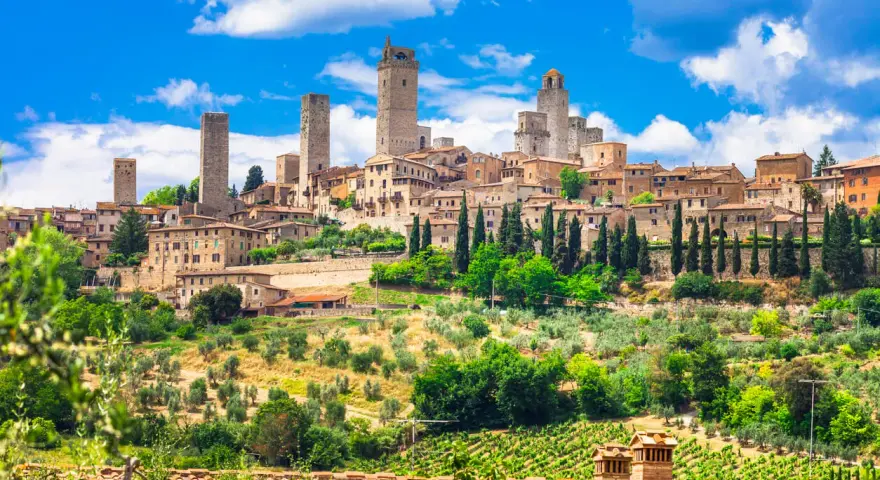 Widok na średniowieczne wieże i zabudowania San Gimignano w Toskanii, otoczone zielenią i winnicami.
