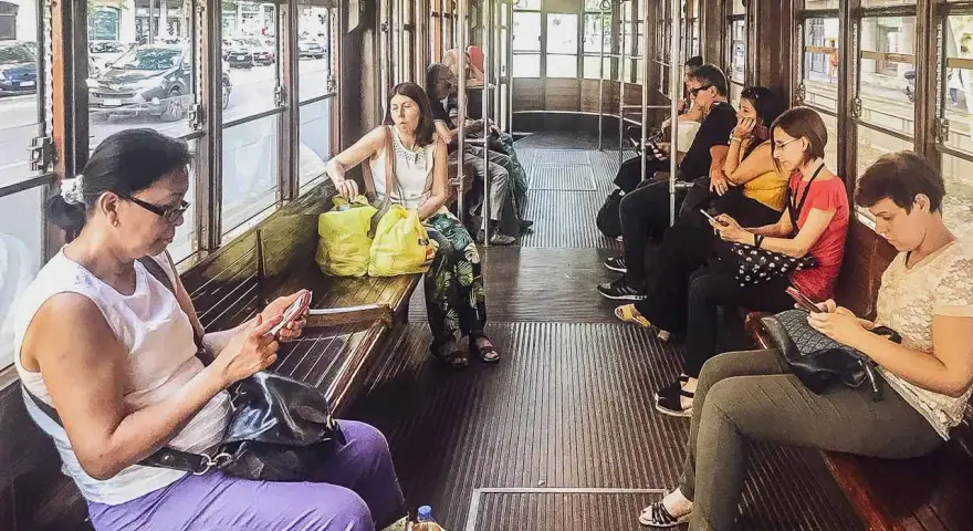 Wnętrze tramwaju w Mediolanie. Pasażerowie korzystają z mediolańskiej komunikacji miejskiej, przeglądając telefony.