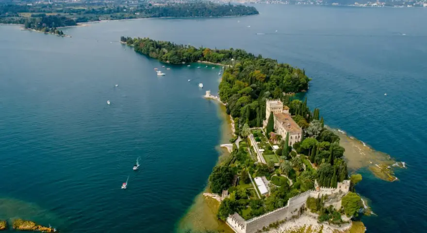 Malowniczy widok na Isola del Garda z pałacem i ogrodami, otoczony turkusową wodą jeziora.
