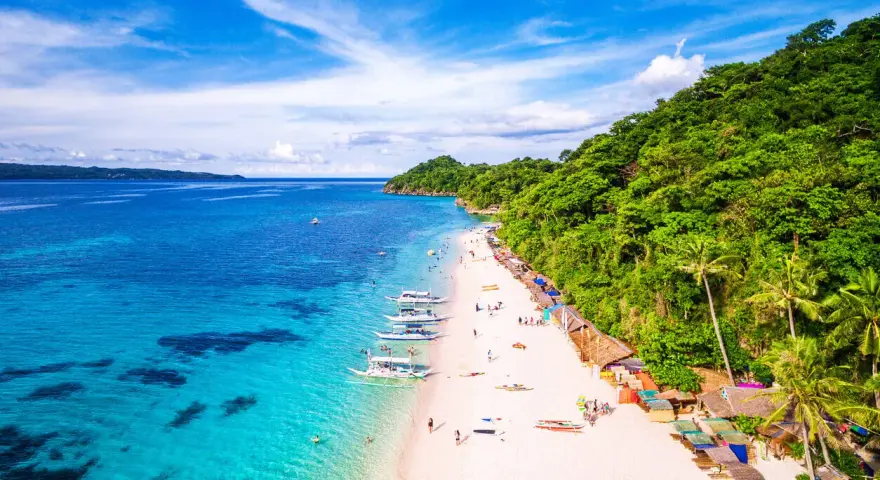 Rajska plaża na Filipinach z turkusową wodą, białym piaskiem, łodziami i zielonymi wzgórzami.