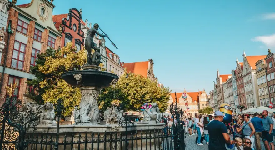 Fontanna Neptuna na tle kamienic i tłumu ludzi w Gdańsku.