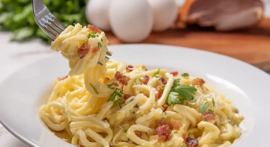 Pyszne spaghetti carbonara przepis na talerzu, z widocznymi jajkami i boczkiem w tle. Idealne danie dla miłośników włoskiej kuchni.