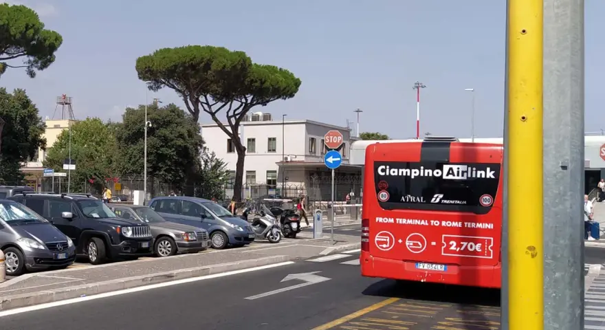 Czerwony autobus Ciampino Airlink na tle parkingu i budynków.