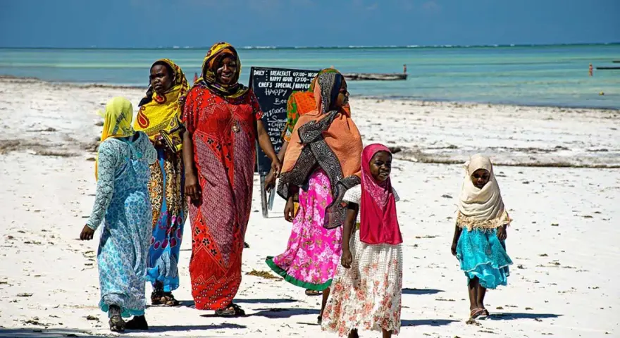 Kobiety w kolorowych strojach spacerują po plaży Zanzibaru. Warto wiedzieć, że to miejsce oferuje piękne widoki i lokalną kulturę.
