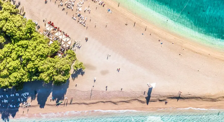 Chorwacja plaże piaszczyste, z turkusową wodą i zielonymi drzewami. Leżaki i parasole czekają na plażowiczów.
