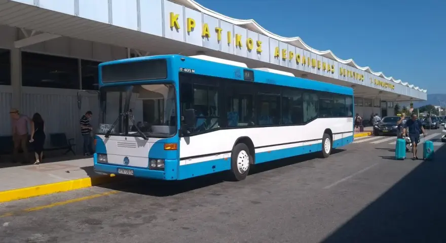 Niebiesko-biały autobus na tle budynku lotniska z żółtym napisem.