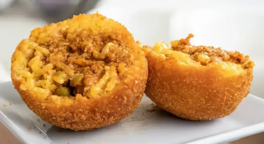 Arancini co to? Chrupiące kulki ryżowe z mięsnym farszem i groszkiem, przekrojone na pół, prezentują swoje bogate wnętrze.