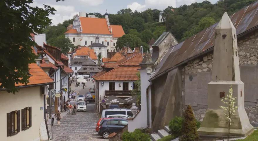 Widok na urokliwą, brukowaną uliczkę Kazimierza Dolnego z zabytkową architekturą i kościołem w tle.