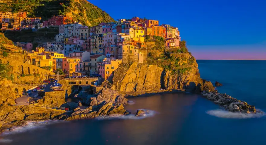 Kolorowe domy Cinque Terre w **Włoszech we wrześniu**, oświetlone złotym słońcem, schodzą ku morzu.