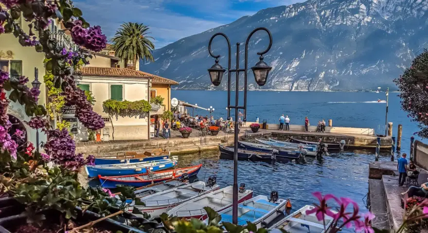 Malowniczy port z łodziami, budynkami i górami w tle nad Jeziorem Garda.