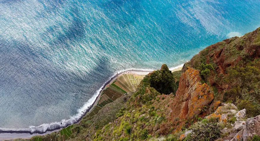 Widok z góry na klif Madery, pola uprawne i ocean.