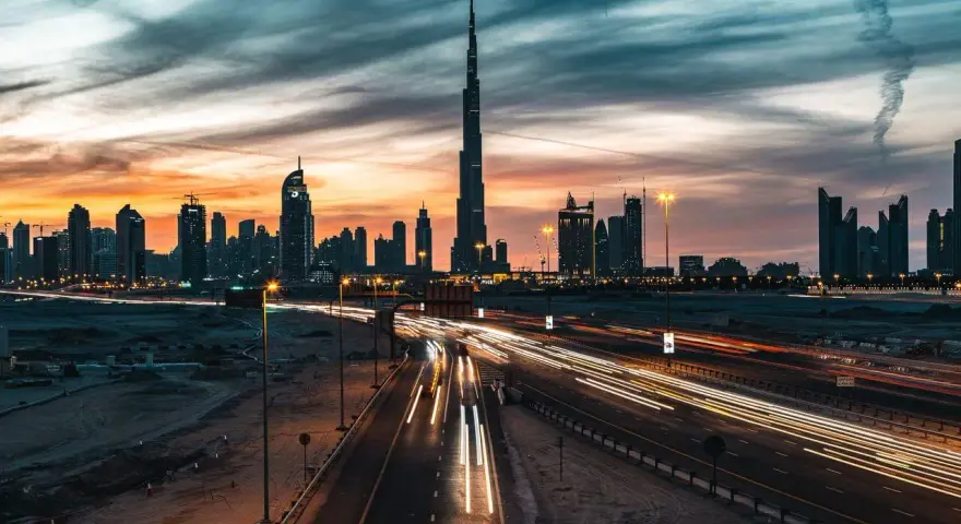 Wieczorny widok na Dubaj z Burj Khalifa, gdzie światła samochodów tworzą smugi na autostradzie. Ciekawostki o tym drapaczu chmur mogą dotyczyć jego wysokości i budowy.