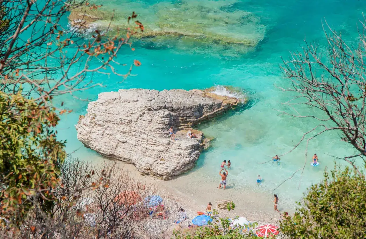 Piękne, turkusowe morze i skalista plaża z ludźmi kąpiącymi się i odpoczywającymi pod parasolami. Idealne fajne miejsca na wakacje za granicą.