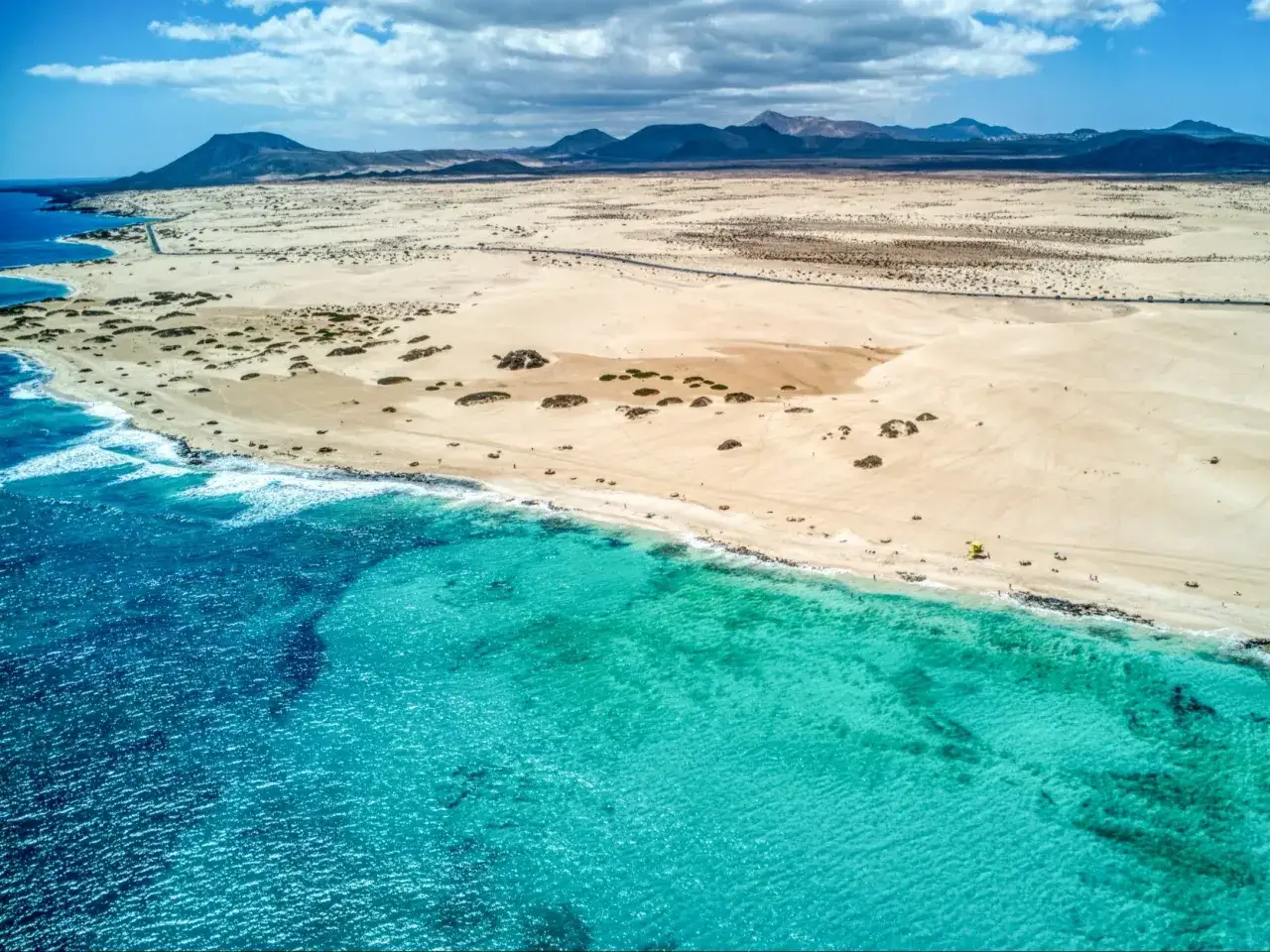 Fuerteventura luty pogoda: piaszczysta plaża, turkusowe morze i górzysty krajobraz. Słoneczny dzień zachęca do spacerów.