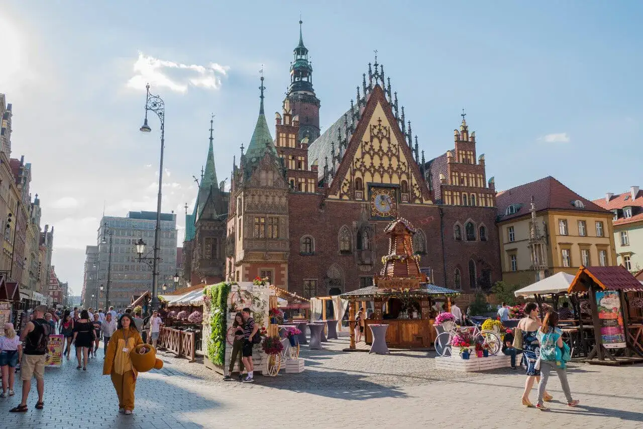 Rynek we Wrocławiu tętni życiem. Ludzie spacerują wśród straganów, podziwiając architekturę. To jedno z wrocławskich ciekawych miejsc.