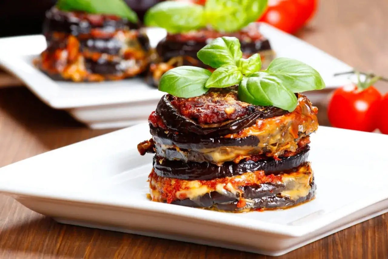 Pyszna parmigiana di melanzane, warstwowa zapiekanka z bakłażana, pomidorów i sera, ozdobiona świeżą bazylią.