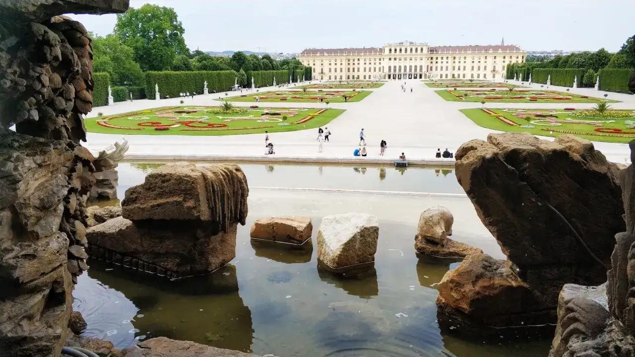 Wiedeń ogrody Sisi: malowniczy widok na pałac Schönbrunn z perspektywy kamiennego wodospadu i stawu.