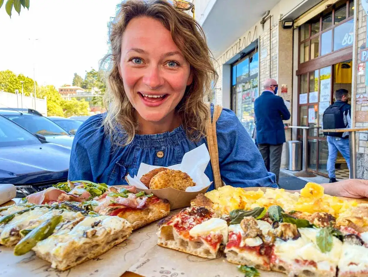 Szukasz miejsca, gdzie zjeść w Rzymie? Ta uśmiechnięta kobieta cieszy się pyszną pizzą i przekąskami na ulicy.