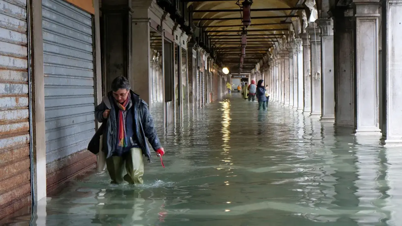 Kobieta w kaloszach przemierza zalane wodą arkady. Acqua alta w Wenecji utrudnia życie mieszkańcom i turystom.
