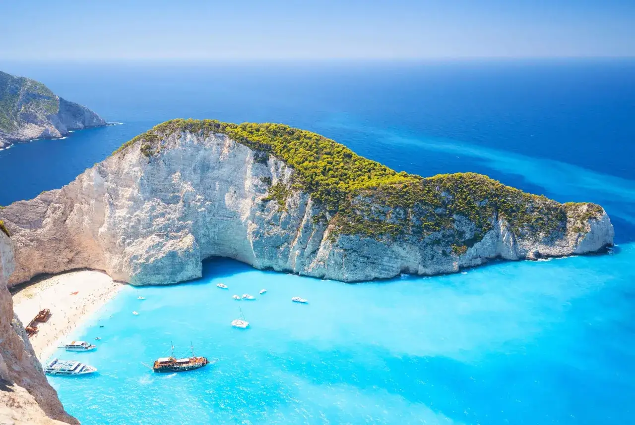 Idealna pogoda na Zakynthos w czerwcu: turkusowa woda, biała plaża i zielone klify.