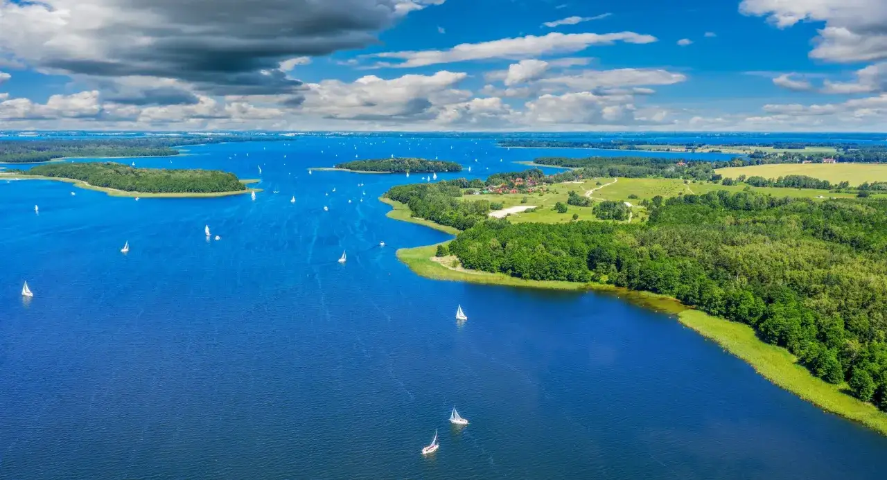 Mazury, gdzie na wakacje w Polsce? Jezioro pełne żaglówek, zielone wyspy i błękitne niebo. Idealne miejsce na relaks i aktywny wypoczynek.