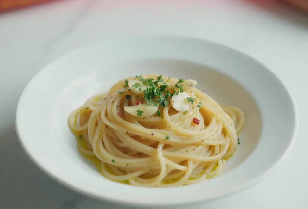 Aksamitne spaghetti aglio olio, udekorowane plasterkami czosnku, natką pietruszki i płatkami chili, skąpane w aromatycznej oliwie.