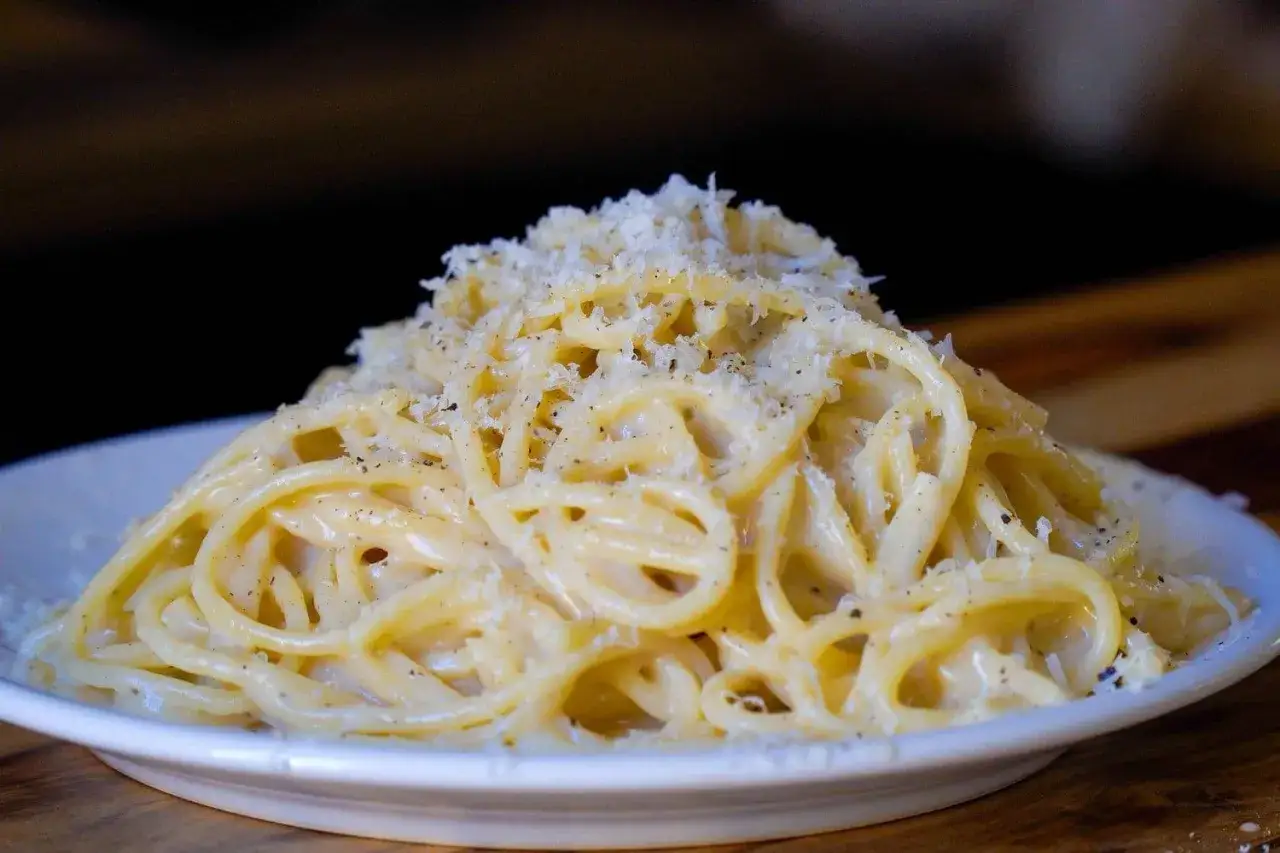 Pyszne spaghetti cacio e pepe, posypane startym parmezanem i świeżo mielonym pieprzem, na białym talerzu.