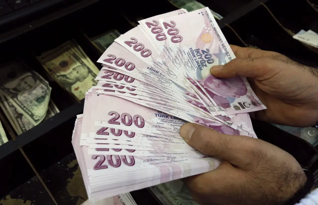 Ręce trzymają stos banknotów po 200 lir tureckich. To właśnie nimi płaci się w Turcji. W tle widać dolary.