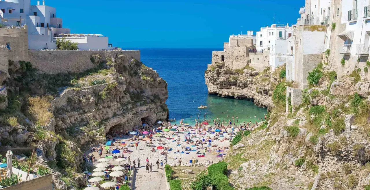 Piękna plaża w Polignano a Mare, idealne miejsce na odpoczynek po podr&oacute;ży z Bari. Woda krystalicznie czysta, a białe domy wznoszą się na klifach.