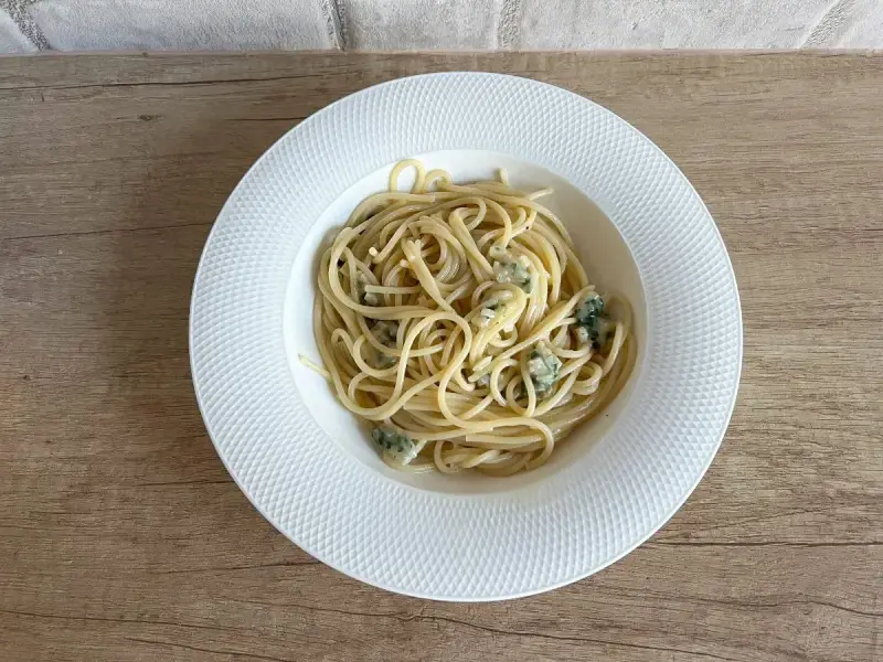 Pyszne spaghetti aglio olio z kawałkami sera pleśniowego na białym talerzu.