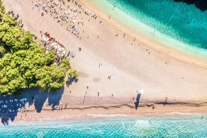 Chorwacja plaże piaszczyste, z turkusową wodą i zielonymi drzewami. Leżaki i parasole czekają na plażowiczów.