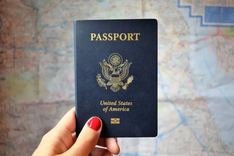 Dłoń trzyma paszport USA na tle mapy. Czas oczekiwania na paszport może być długi, ale podróż warta jest tej chwili.
